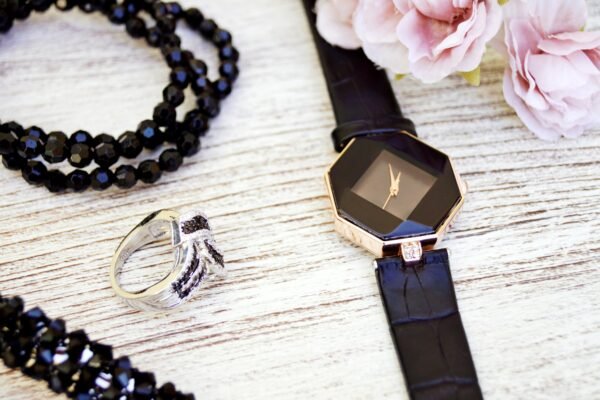 Close-up of luxurious black jewelry and watch with pink flowers on a wooden surface.