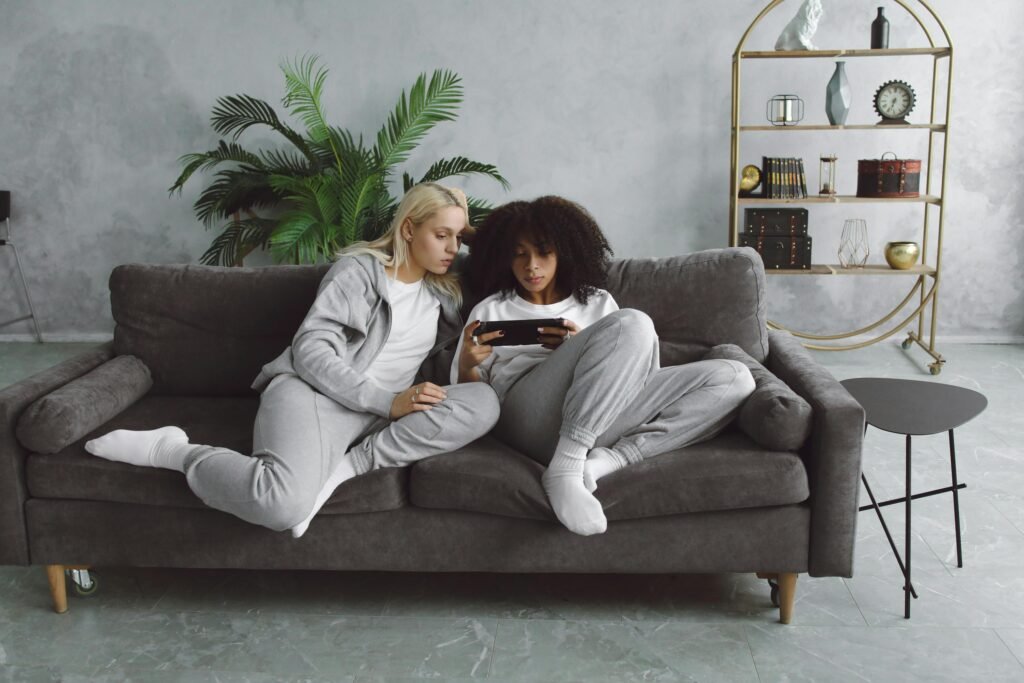 Two women in cozy loungewear enjoying video games together on a sofa.